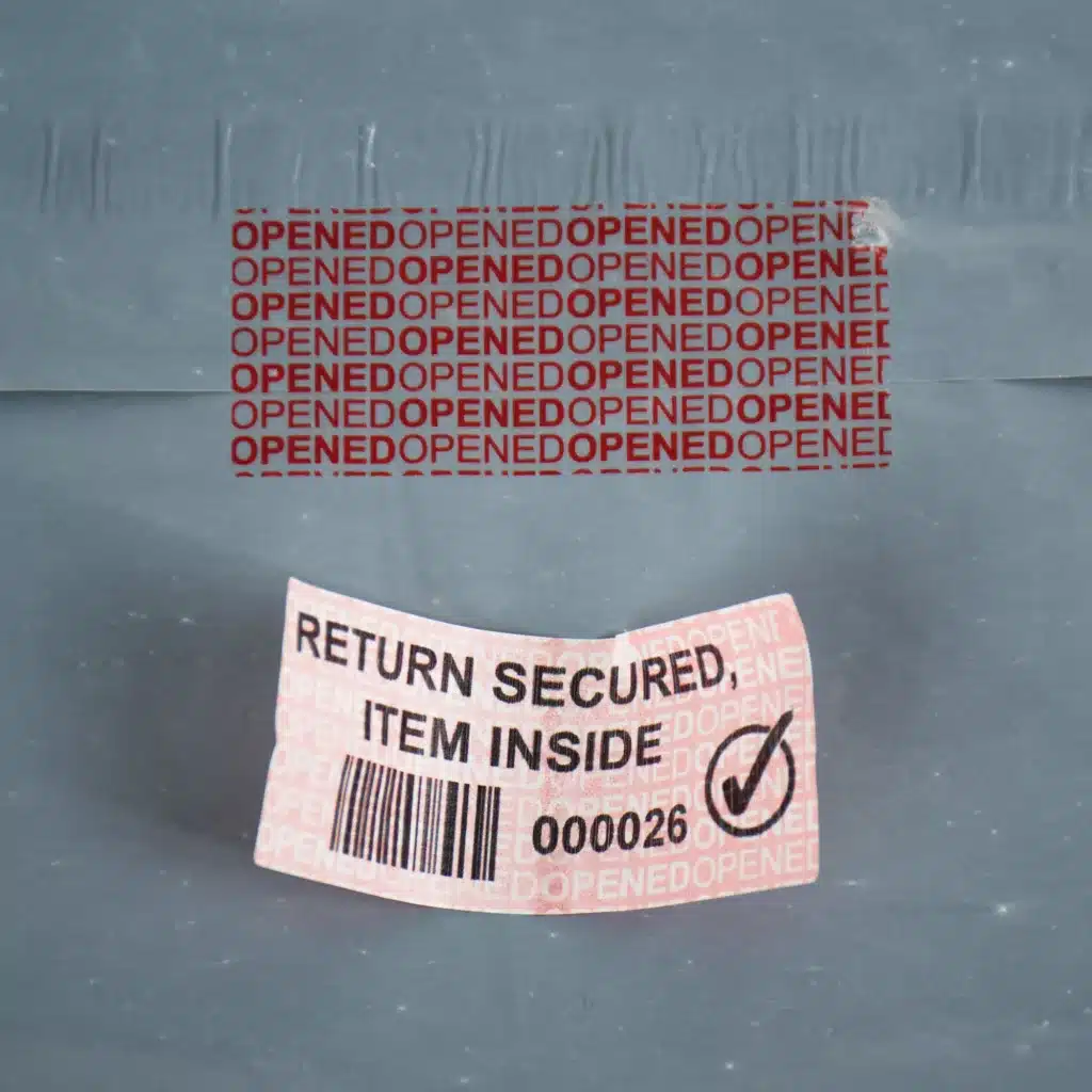 Image of E-Commerce permanent red paper tamper evident label removed from a bag showing "OPENED OPENED" void message and the label after it has been removed
