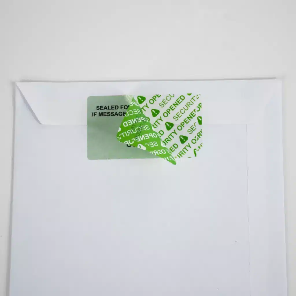 Image of a Secure Item permanent green paper tamper evident label half removed from an envelope showing "SECURITY OPENED" void message