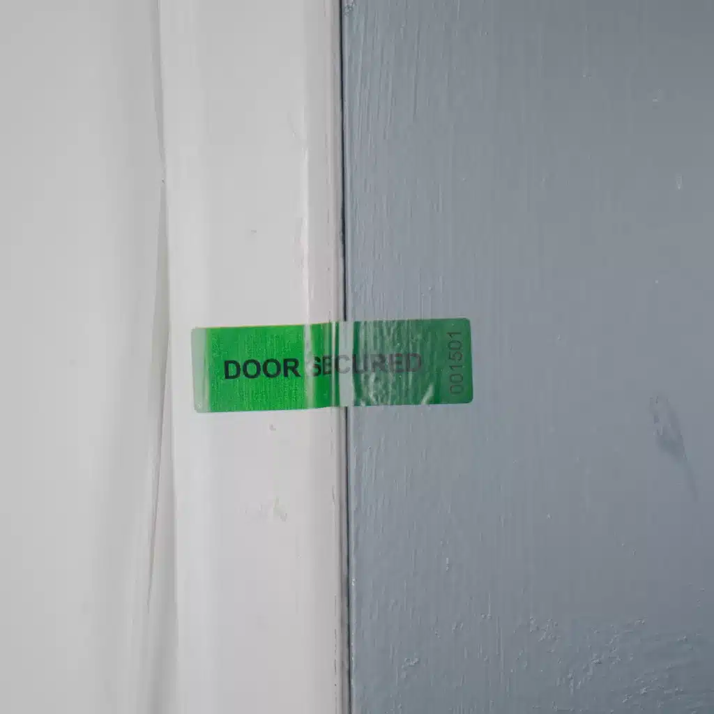 Image of a roll of green Tampertech tamper evident Door Secured non-residue label applied to a door and door frame.